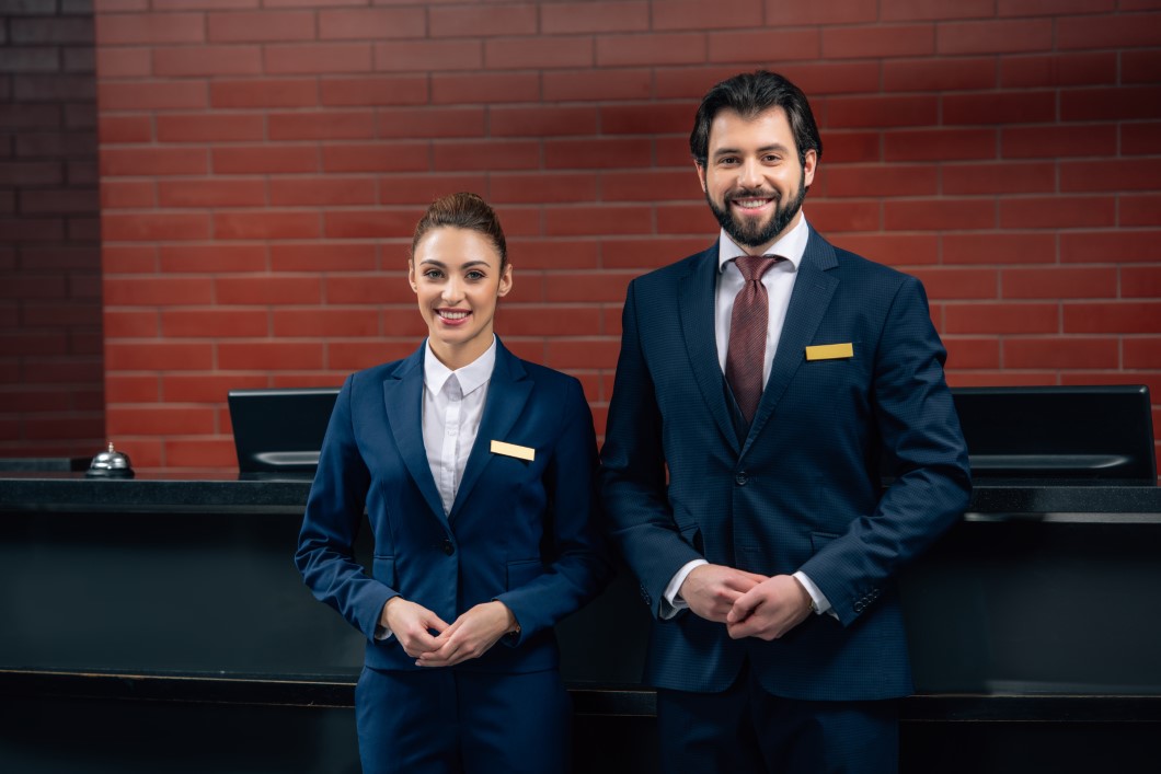 hotel receptionists standing together in front of counter and looking at camera