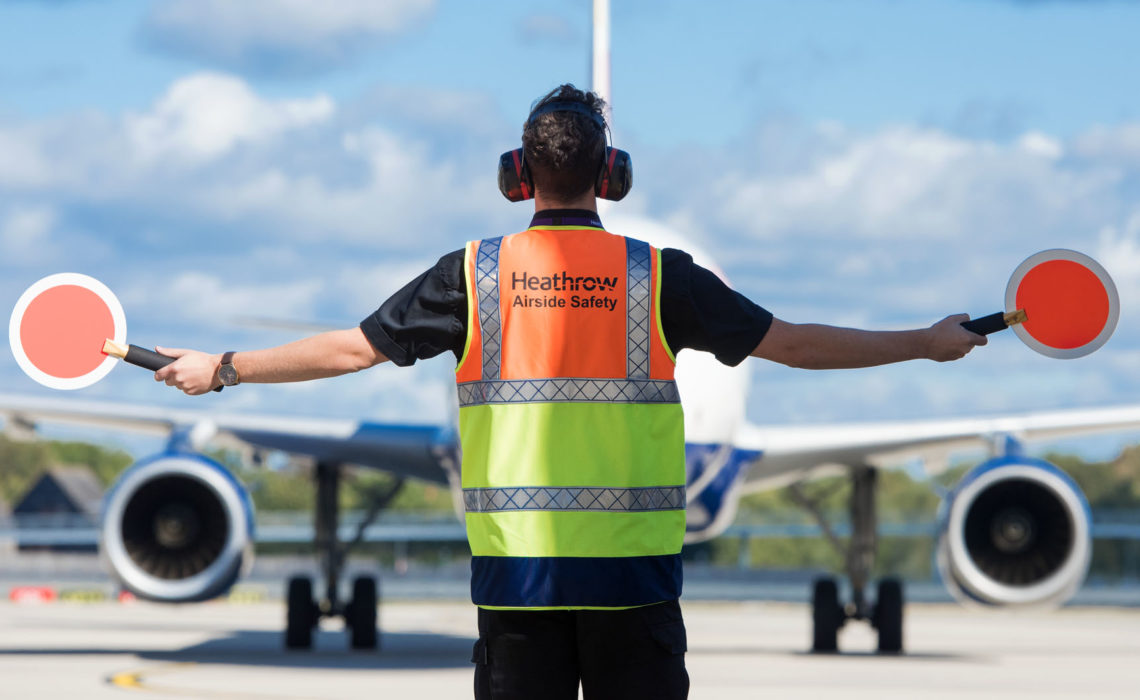 Heathrow, airfield, airfield ops marshaller guiding aircraft on apron, Sep 2018.