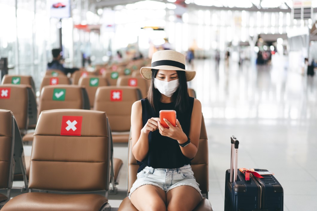 Young adult tourist woman wear mask for virus outbreak at airport terminal with social distancing chair.